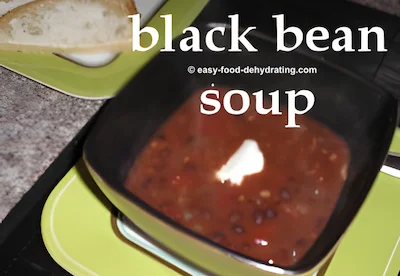 Black bean soup with a blob of sour cream, in a square bowl on a green square plate