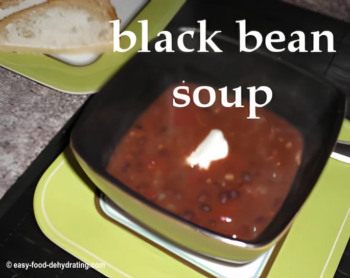 Black Bean soup with a dollop of sour cream in a square bowl with a dark interior