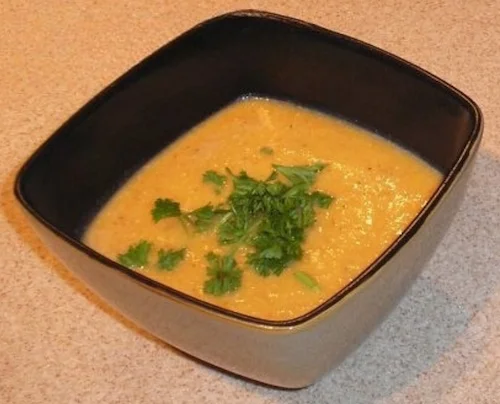 Creamy carrot soup in a black bowl topped with parsley.