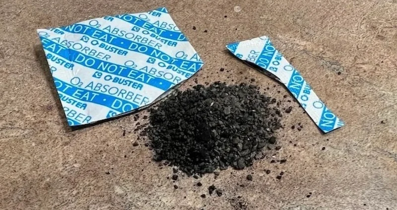 Cut open oxygen absorber packet showing dark granular iron powder contents