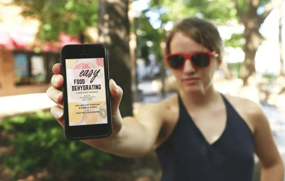 Easy Food Dehydrating & Safe Food Storage eBook shown on a cellphone, held outstretched by a female