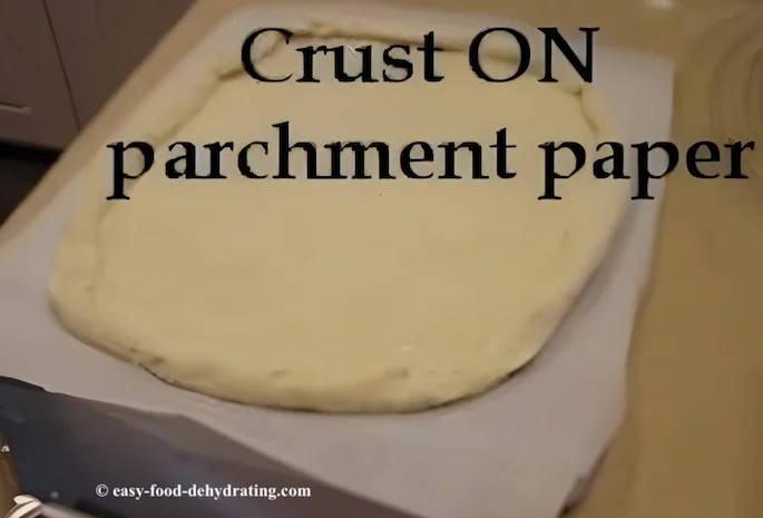 Pizza crust on parchment paper, atop a huge spatula Pizza ready to bake - no parchment paper is needed after pre-baking