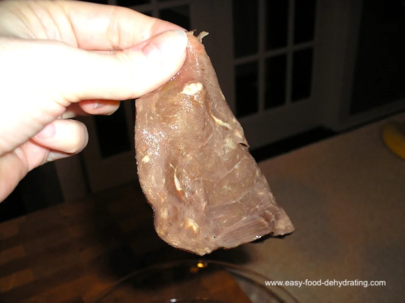Hand holding a limp piece of rehydrated beef strip.