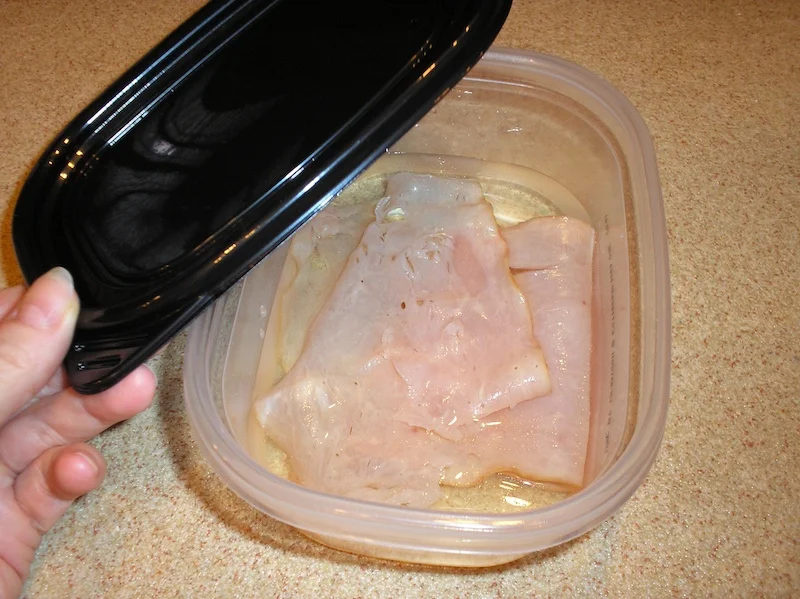 Slices of dehydrated deli turkey rehydrating in a plastic container of cold water inside the fridge.