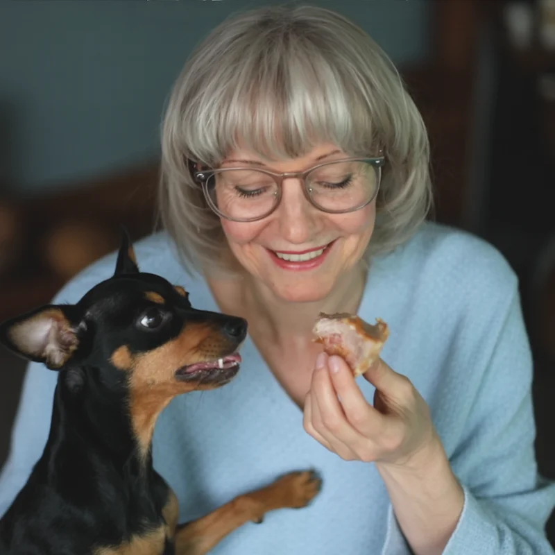 Smiling woman holding a dehydrated turkey treat while her dog eagerly waits for a bite