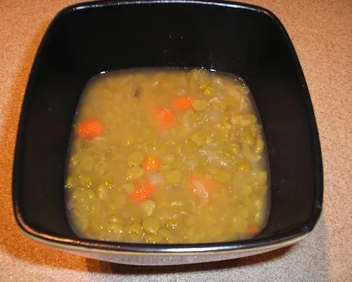 Hearty split pea soup with carrots served in a black bowl.